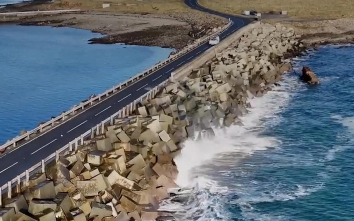 A road along a causeway of concrete blocks with surf breaking against it