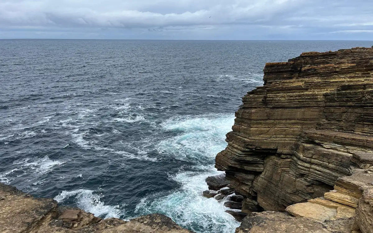 Layered sandstone cliffs with waves breaking at their foot