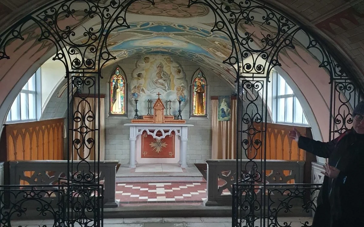 A painted chapel altar seen through an ornate wrought-iron screen