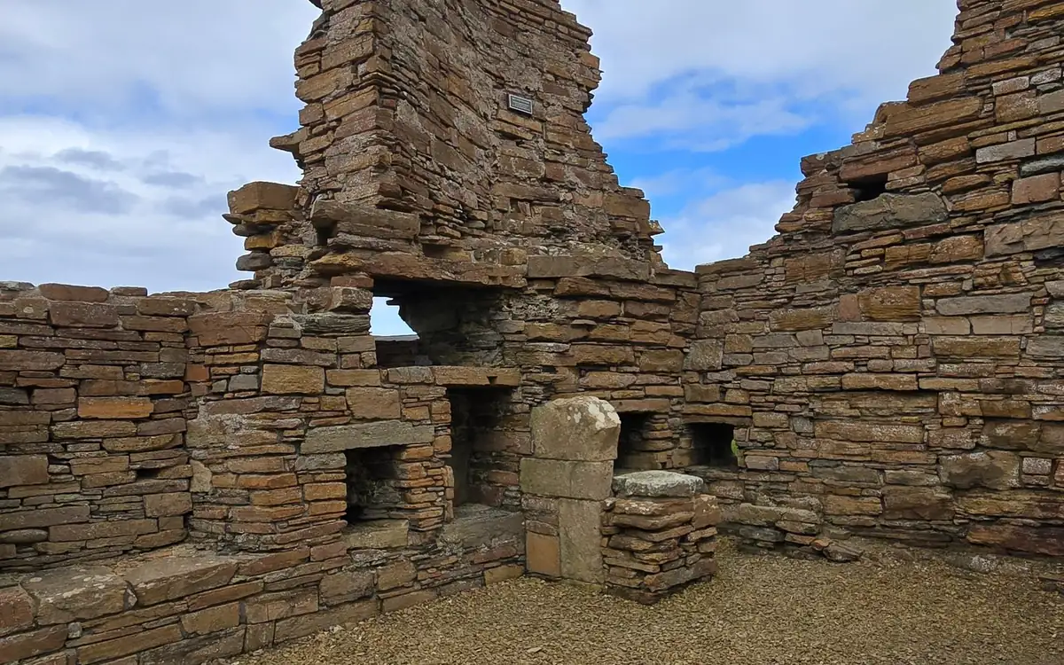 Roofless ruins of a palace built of flat stone, with small niches in the walls