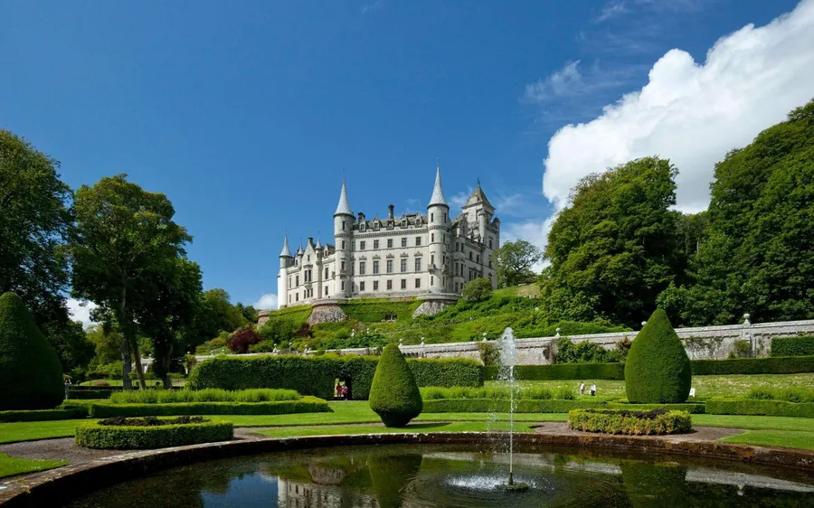 A white castle with pointed turrets above formal gardens and a fountain pool