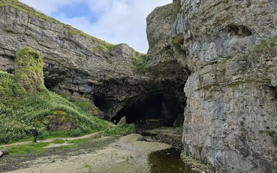 Grey cliffs above a shallow stream, a walker on the path below