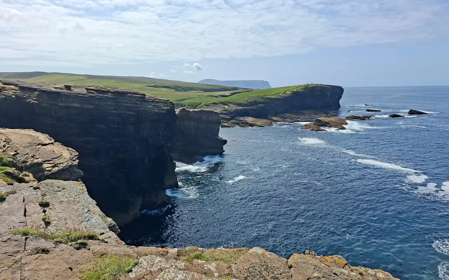 Dark layered sea cliffs above deep blue water, a green headland beyond