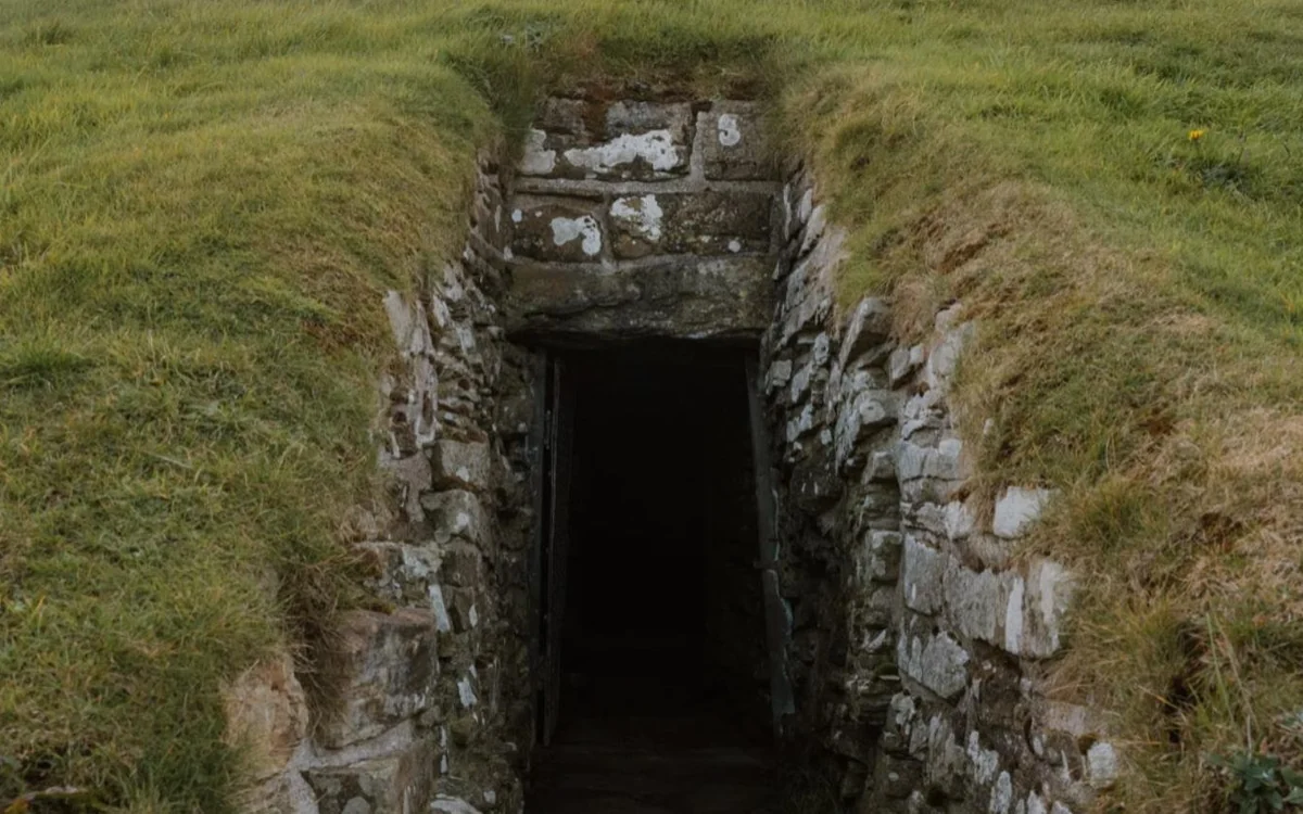 A low stone-lined passage leading into a grassy burial mound