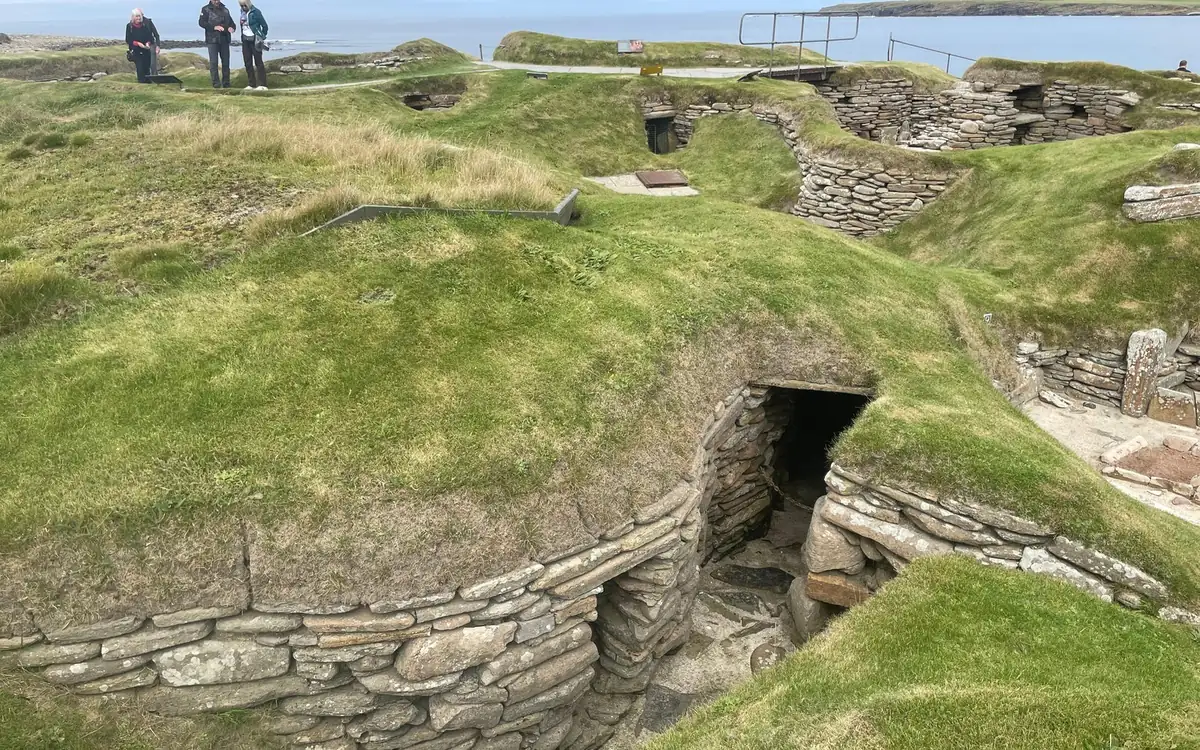A stone-walled passage between grassed-over sunken houses of a Neolithic village