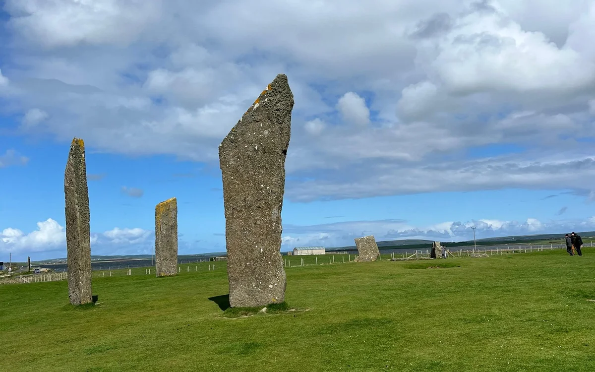 Tall thin standing stones on mown grass under a cloudy sky