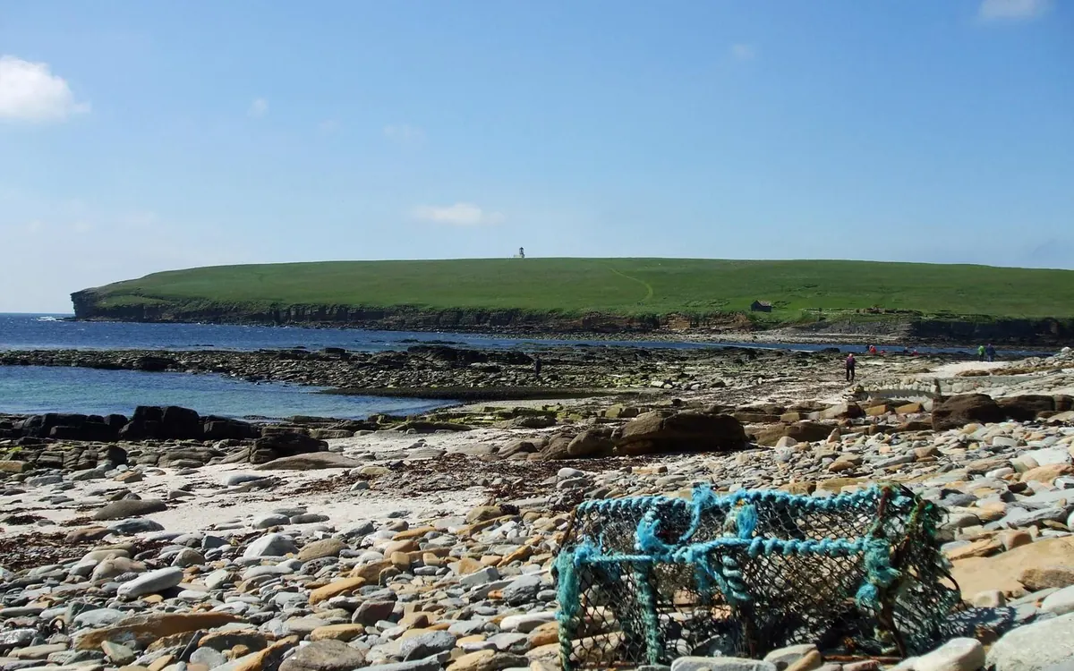 A low green tidal island seen across a rocky shore with lobster creels