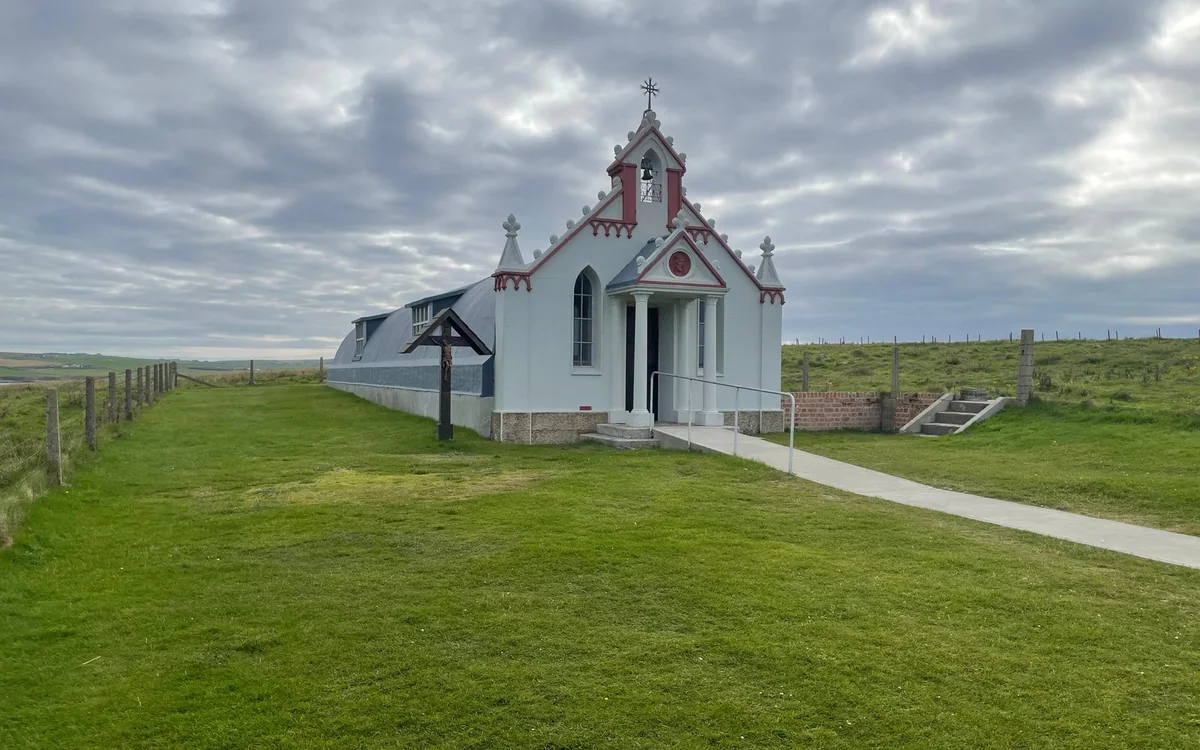 The white painted front of a small chapel on a green lawn