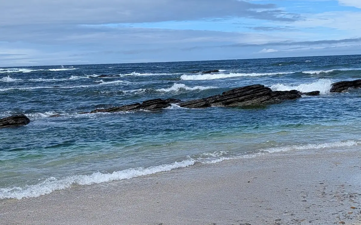 Pale sand and breaking waves, with ledges of dark rock in the water